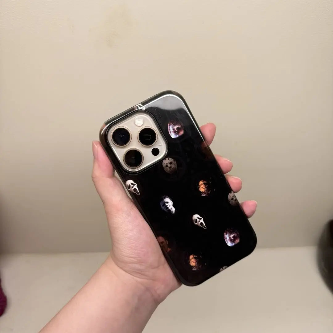 This Halloween phone case features classic horror movie character faces on a black background, offering a subtle yet mysterious vibe for your phone.