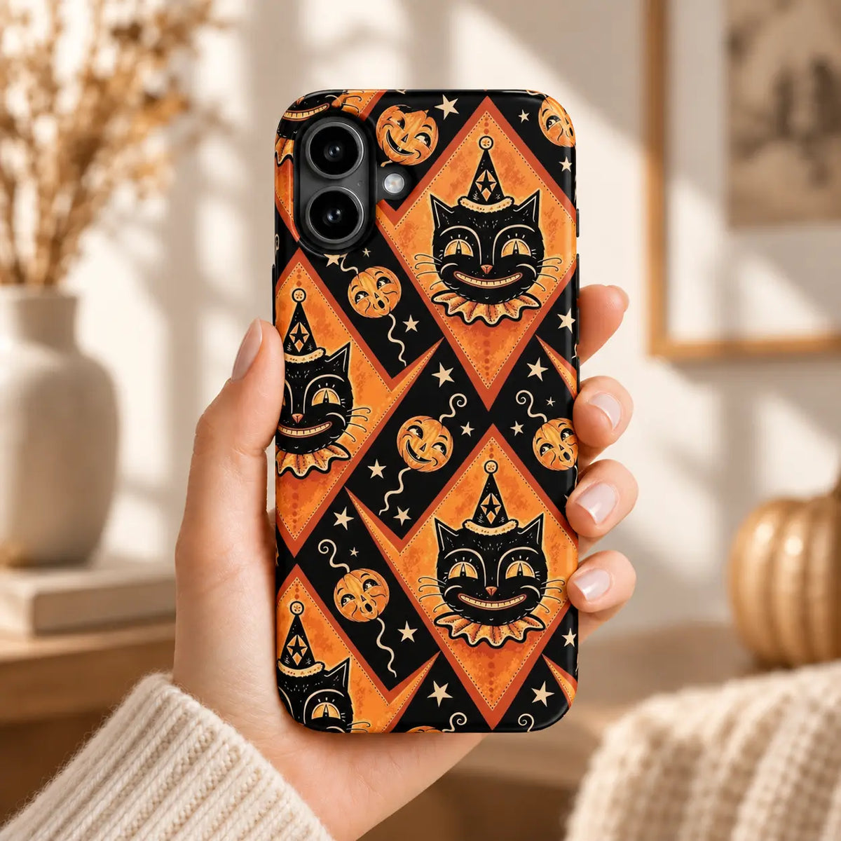 Hand holding an iPhone with a vintage Joker Cat case featuring cats in clown hats, orange diamonds and pumpkins