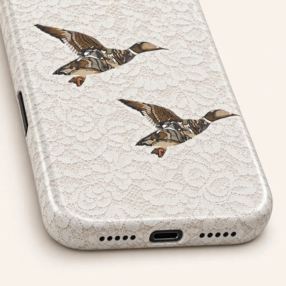 iPhone bottom close-up showing charging and speaker openings: white floral lace print; two camouflage ducks.