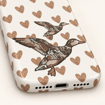 iPhone bottom close-up showing charging and speaker openings: white background with sketch-style tan hearts; two flying ducks, one large and one small.