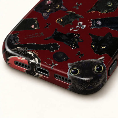 Close-up of the phone case's bottom edge and port openings beneath large black cat faces on a burgundy background