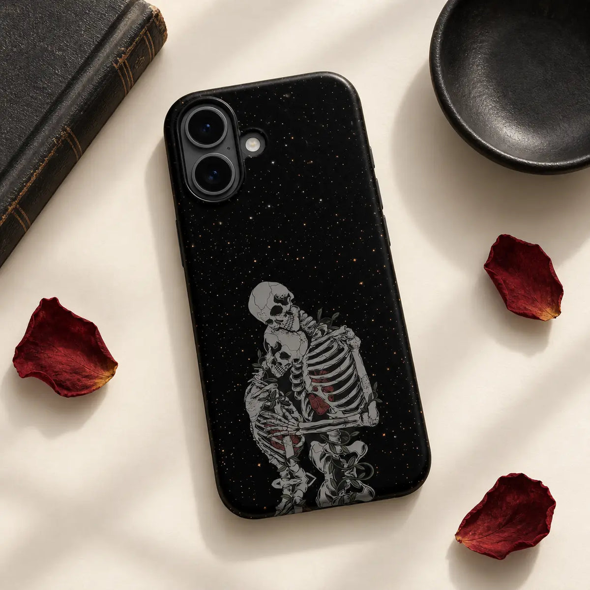 Embrace skeleton phone case styled with dark book and dried red petals