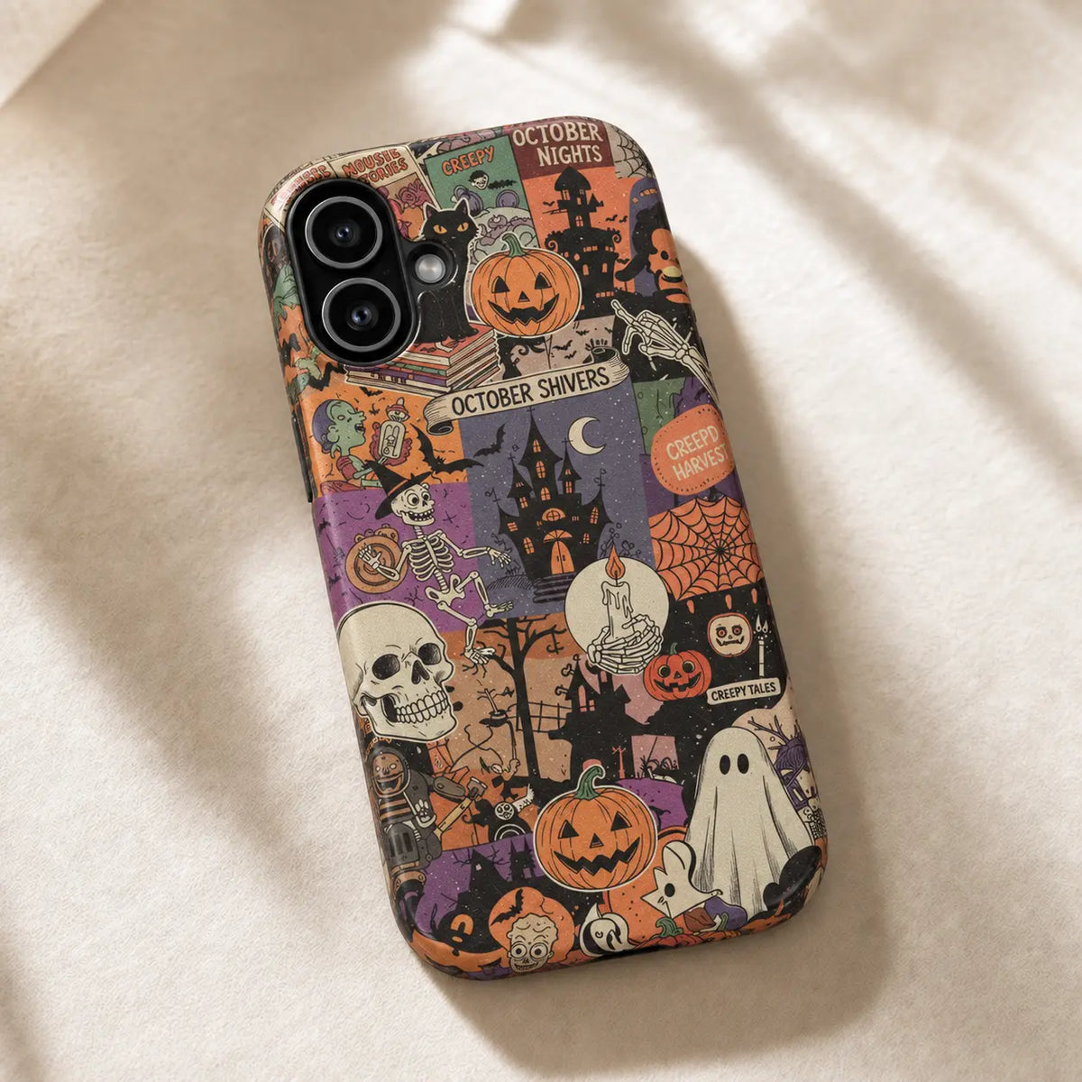 Vintage Halloween collage iPhone case resting on cream fabric in sunlight, showing pumpkins, skeletons and haunted houses