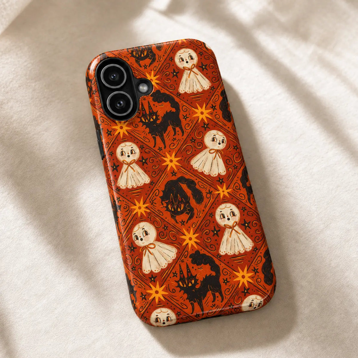 Orange vintage ghost and black cat iPhone case resting on cream fabric in warm sunlight