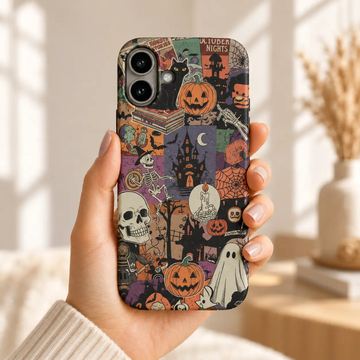 Hand holding an iPhone with a vintage Halloween collage case featuring orange pumpkins, a cream ghost and a black cat