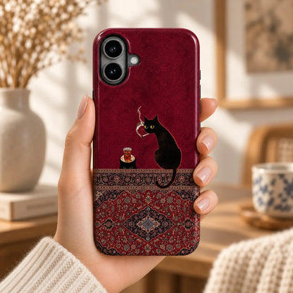 Hand holding an iPhone with a burgundy case featuring black cats, a tea glass and an ornate Persian rug design