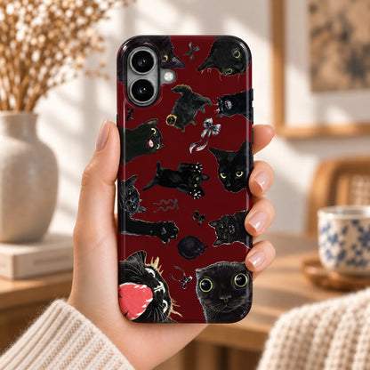 Hand holding an iPhone with a burgundy case covered in funny black cat portraits and ribbon bows