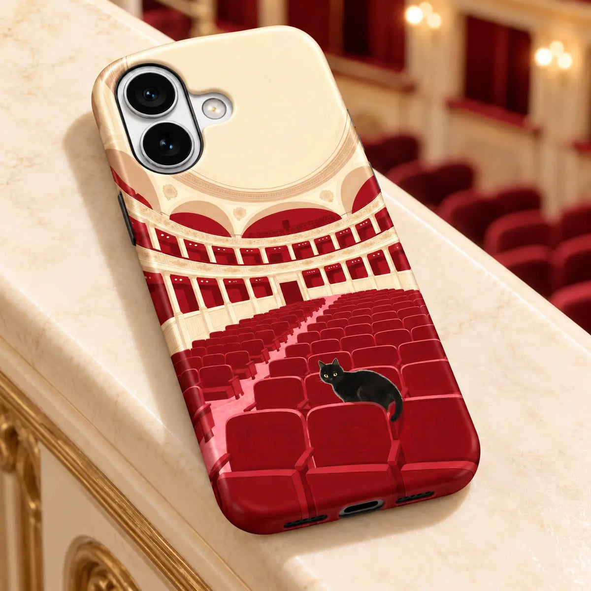 iPhone case on an ivory ledge with theater seating behind; Black cat among red theater seats with cream balconies