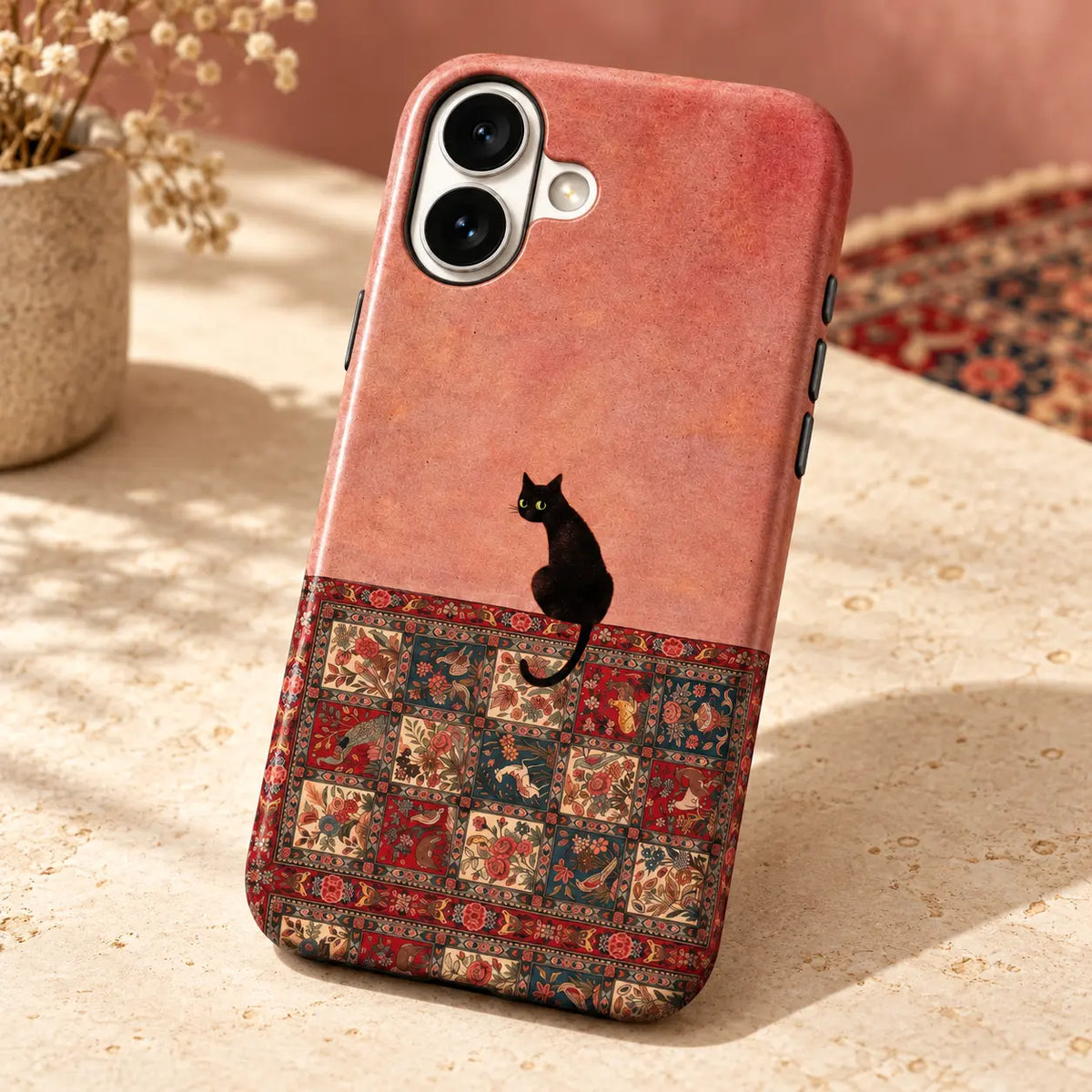 iPhone case on an ivory tabletop; Black cat above a red, cream and deep teal floral bird rug print
